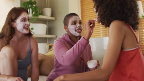 grupo diverso de felices amigas intentando maquillaje y hablando en casa