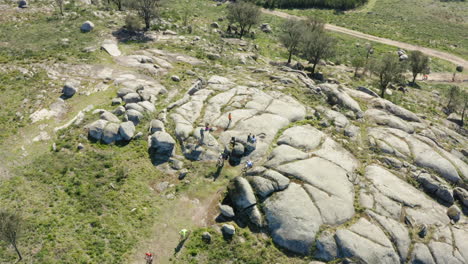 cyclists gathering in mountain peak large boulder in minho, portugal - aerial top orbit shot