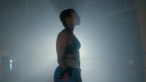 side view of a young caucasian sportswoman with braided pigtails jumping rope in boxing ring