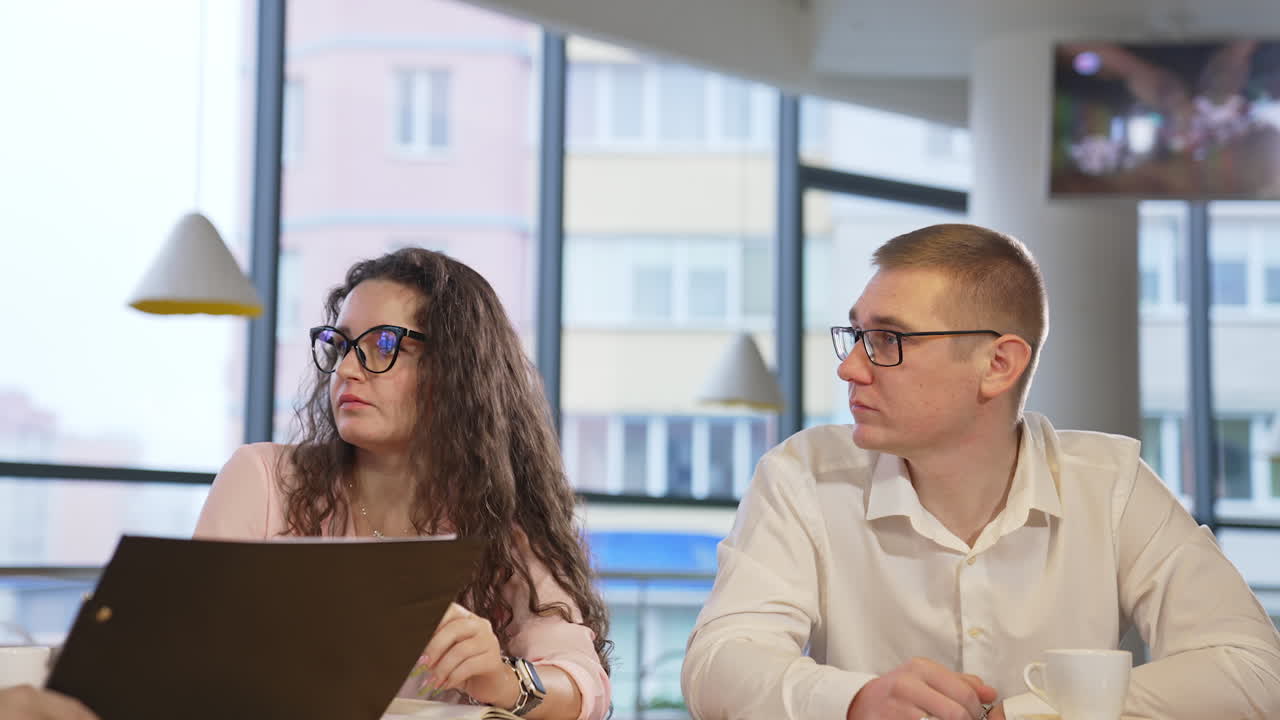 Business people at the work meeting sitting at the table. Two employees look puzzled listening to the speaker. Blurred backdrop.