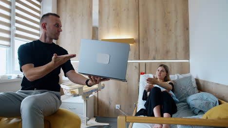 Caucasian couple having a newborn in the maternity hospital. Woman breastfeeding a baby and husband shows her something on laptop.