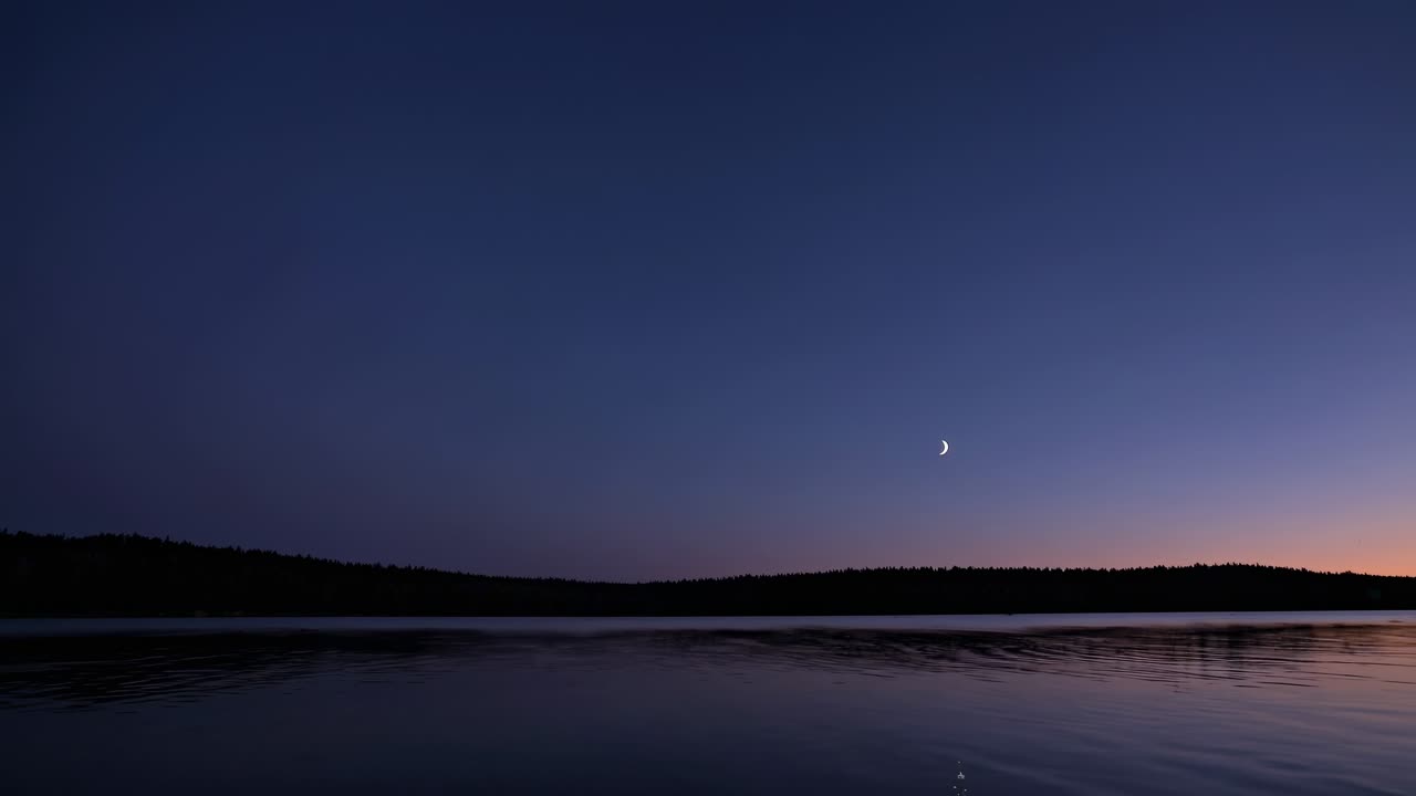 A serene twilight video scene with a crescent moon over a calm lake