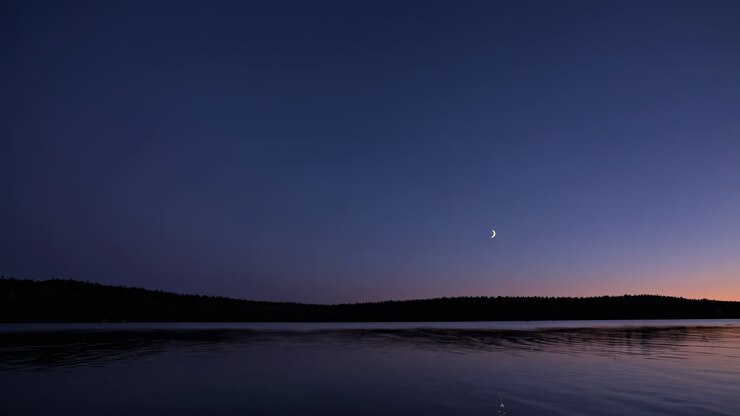 Una serena scena video al crepuscolo con una luna crescente su un lago calmo