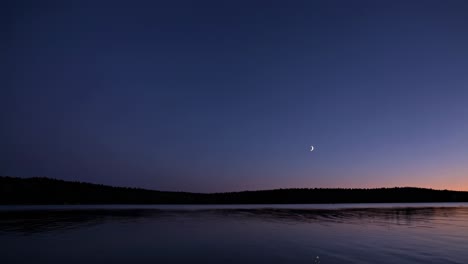 A serene twilight video scene with a crescent moon over a calm lake