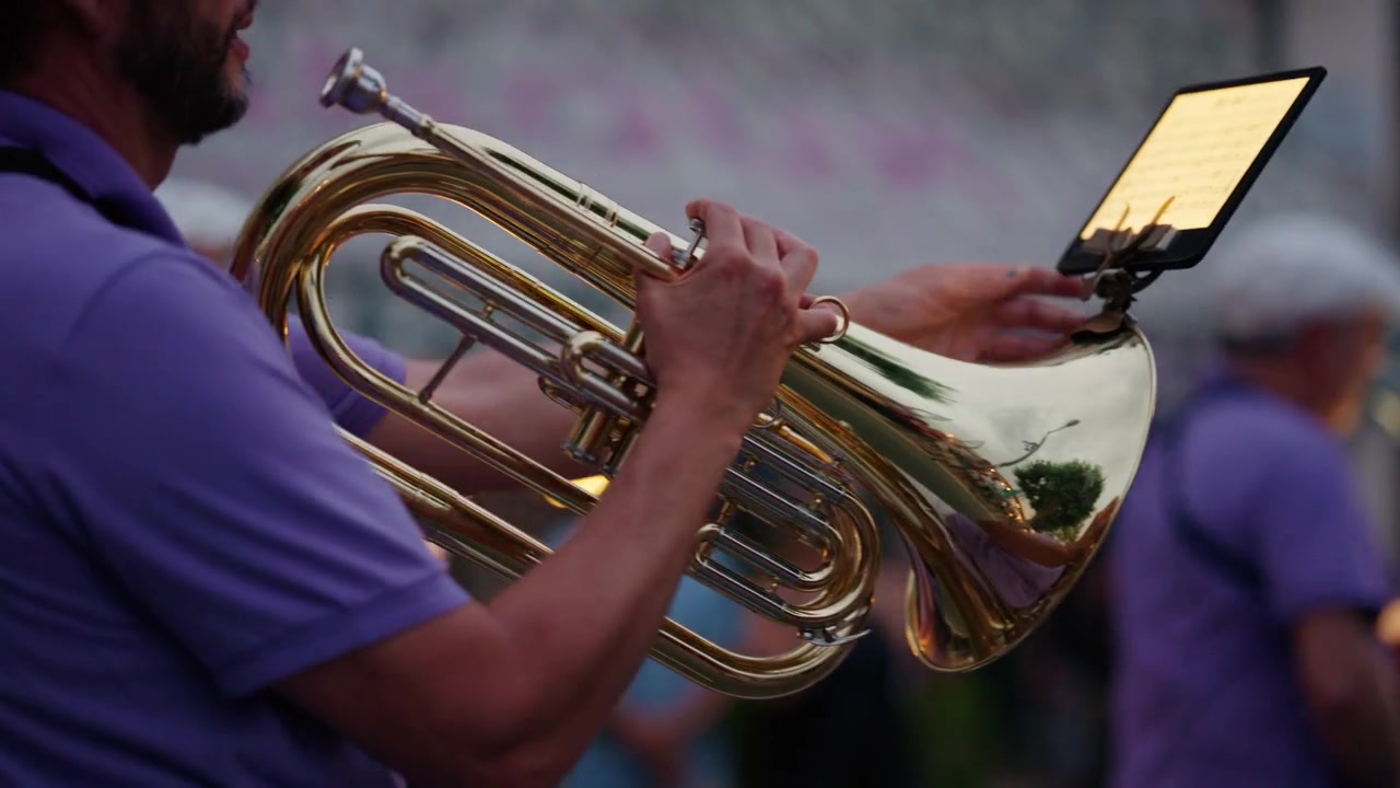 Musicista che suona uno strumento a fiato durante un concerto all'aperto o una parata. Focus sulle mani del musicista e sullo strumento.