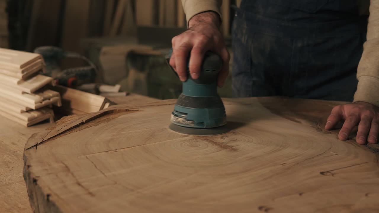 Men's, rude, working hands of carpenter handle the wood with a grinding machine. Checks the smooth surface with the hand