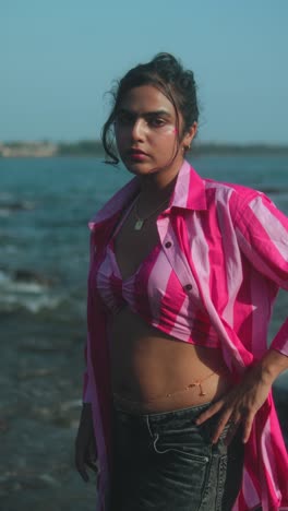 confident, stylish woman posing near the ocean in a striped pink outfit