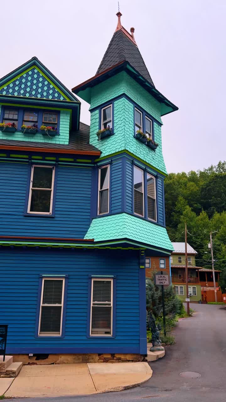 Rumah bergaya Victoria berwarna biru dan toska dengan menara sudut. Pemandangan detail sebuah rumah kayu biru cerah dengan sirap berlekuk berwarna toska dan menara runcing.
