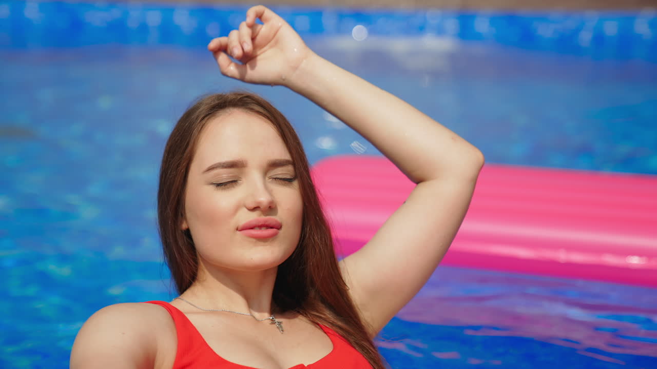 Girl in red top swimming on a swimming circle in a pool. Beautiful lady in a pool enjoying the sun. Blurred backdrop.