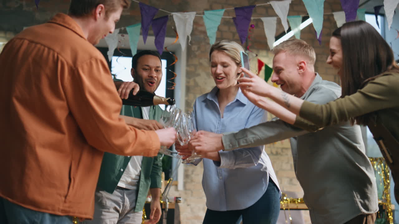 Venner og kolleger hælder champagne i glas til fest. Glad team fejrer.
