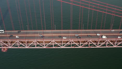 Side-slider-view-of-busy-multi-lane-traffic-across-a-red-bridge-over-the-sea.-Cars-crossing-Ponte-25-de-Abril-suspension-bridge-in-Lisbon,-Portugal