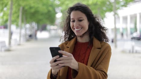 Aufgeregte-Frau,-Die-Im-Freien-Ihr-Mobiltelefon-Benutzt