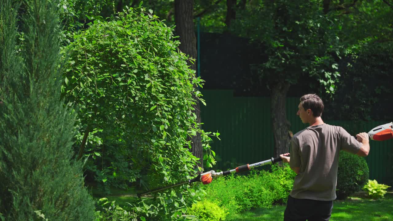 Man Trimming Green Bush with Long-Reach Hedge Trimmer in Garden