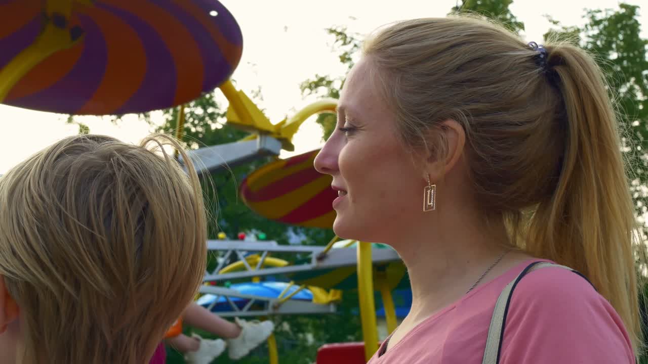 madre y hijo en la feria de atracciones de pie y ver el giro del carrusel, aunque van a montar en él, de pie en la línea. familia feliz en vacaciones