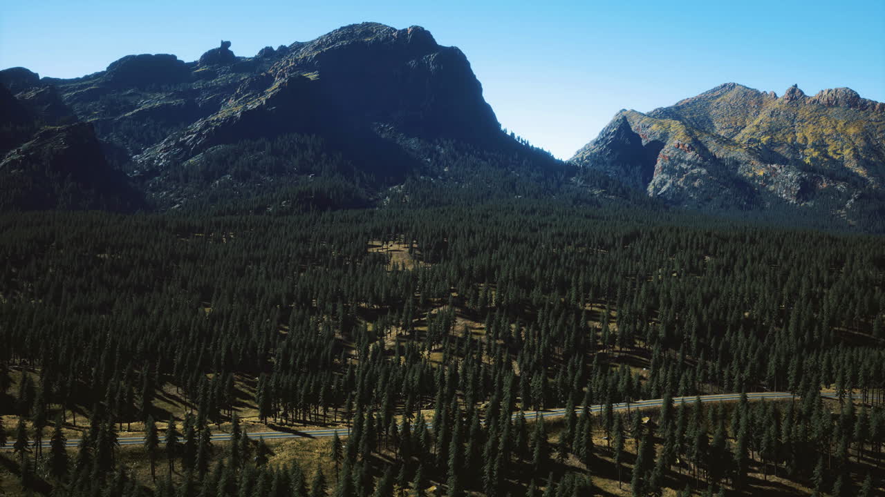 Majestic mountains rise above dense forest under clear blue sky