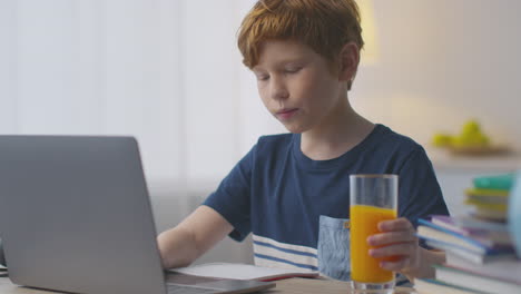 boy drinking orange juice while studying on laptop