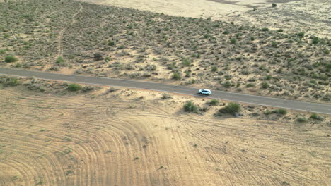 tomada de un avión no tripulado de 4k de un coche que avanza por la carretera de longewala, rodeado por el desierto dorado de jaisalmer. las interminables arenas y vegetación en un día soleado de rajasthan