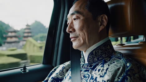 senior man in formal clothing views scenic asian landscape from car window
