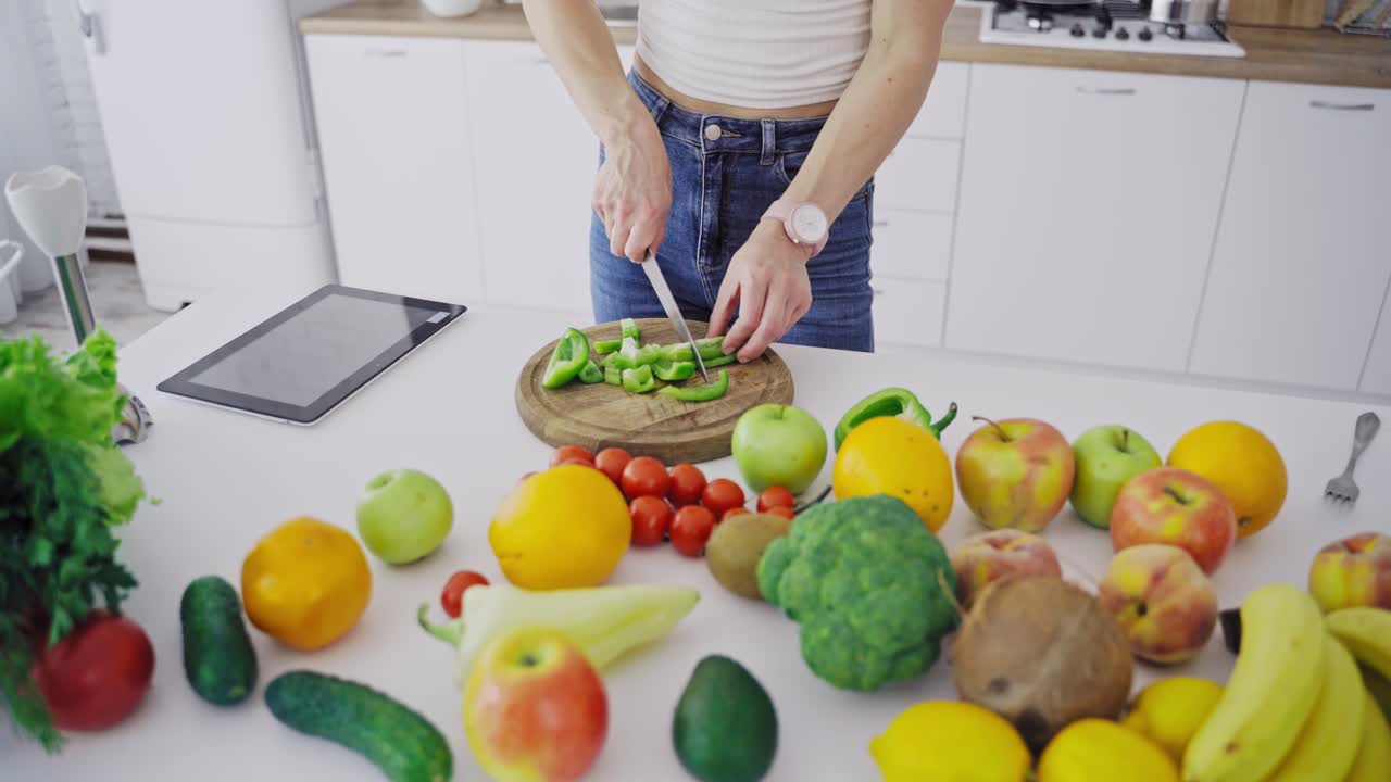 Organic vegetables and fruit on the table. Woman is cutting green pepper on a wooden board to prepare healthy food. Dieting concept.