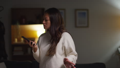 angry anxious or stressed woman spending evening at home standing in lounge talking on mobile phone