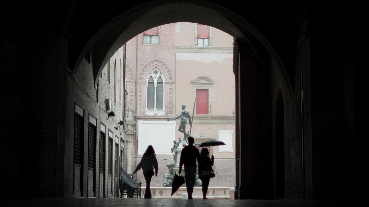 Turisti e residenti si riparano dalla pioggia mentre camminano per Piazza del Nettuno a Bologna, Italia