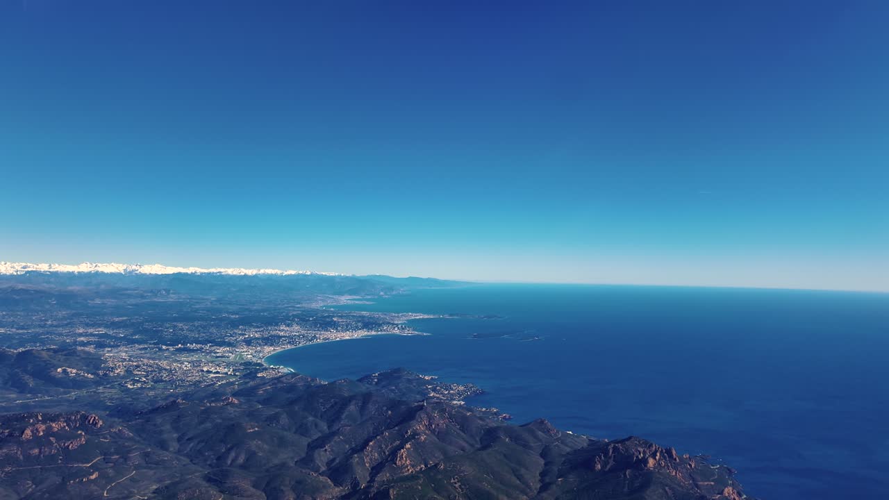Riviera Prancis dari langit dengan Pegunungan Alpen yang tertutup salju di latar belakang, direkam dari kokpit pesawat yang terbang di atas Cap Rouge, dekat Nice (NCE) pada hari musim dingin yang cerah.