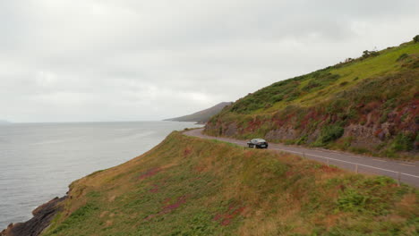 Forwards-tracking-of-car-on-coastal-road-on-cloudy-day.-Rocky-sea-coast-with-cliffs-and-grassy-slope.-Ireland