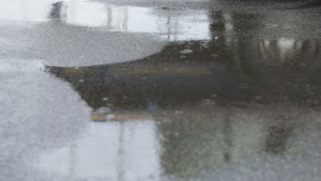 Reflection-of-a-passing-truck-in-water-on-the-tar-road-as-rain-drizzles-at-a-steady-pace,-street-in-ireland