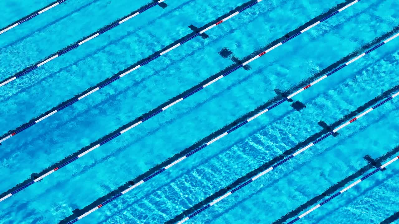 Drone footage captures swimmers in lanes, creating dynamic water patterns under bright sunlight