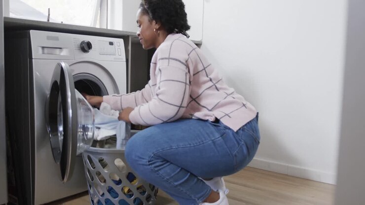 African american woman doing laundry, taking clean clothes out of washing machine, slow motion