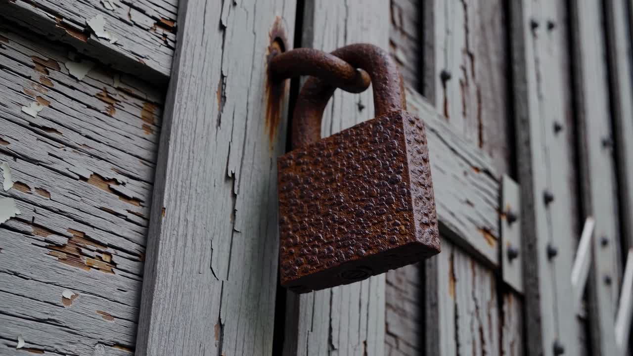 Video ravvicinato di un lucchetto arrugginito su una porta di legno stagionata, ripreso da un'angolazione bassa.