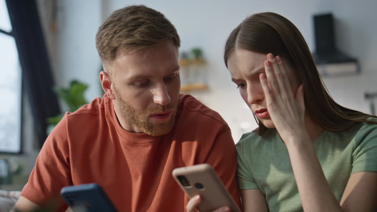 Spouses worried smartphone message sitting living room closeup. Serious family