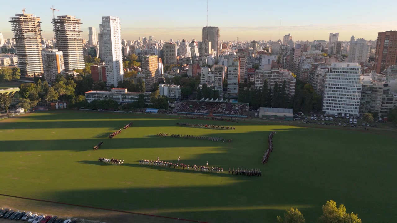 Vista aerea dell'esercito di cavalleria argentino in formazione cerimoniale su un campo da polo al tramonto.