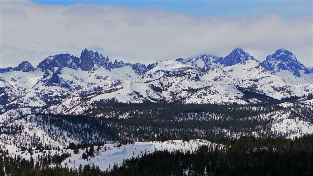 Banner peak Minaret Summit Pass Mammoth Mountains vista Parallax winter aerial drone California group jagged towering snow covered peaks sunny storm Inyo forest Sierra Nevada valley forward pan up
