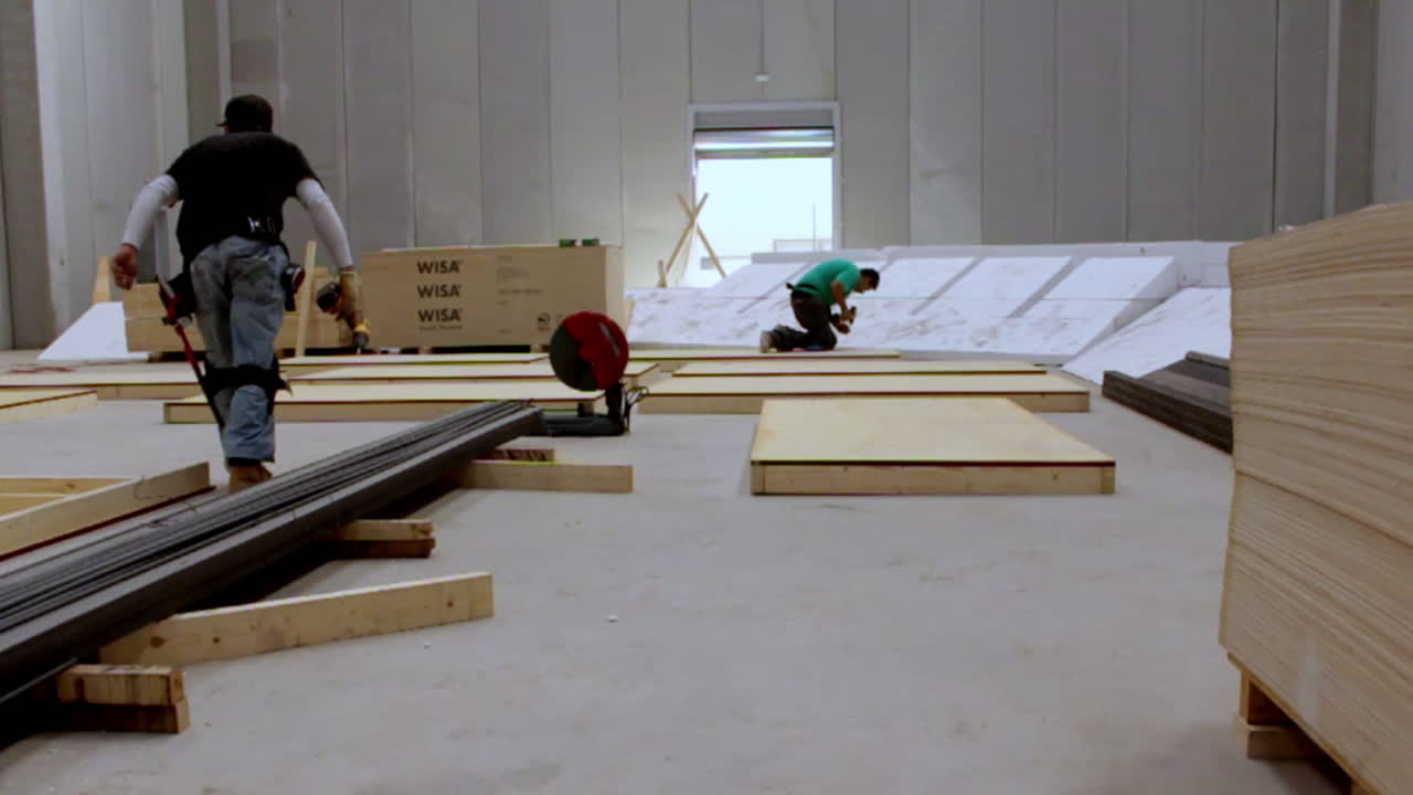 Two workers prepare wood and steel inside a spacious warehouse, evoking concentration, precision, and the raw beauty of organized labor in progress.
