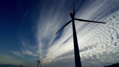 Close-shot-of-a-windmill-in-contrast-to-the-sunny-blue-sky-with-clouds,-its-fins-move-slowly,-countryside-feeling