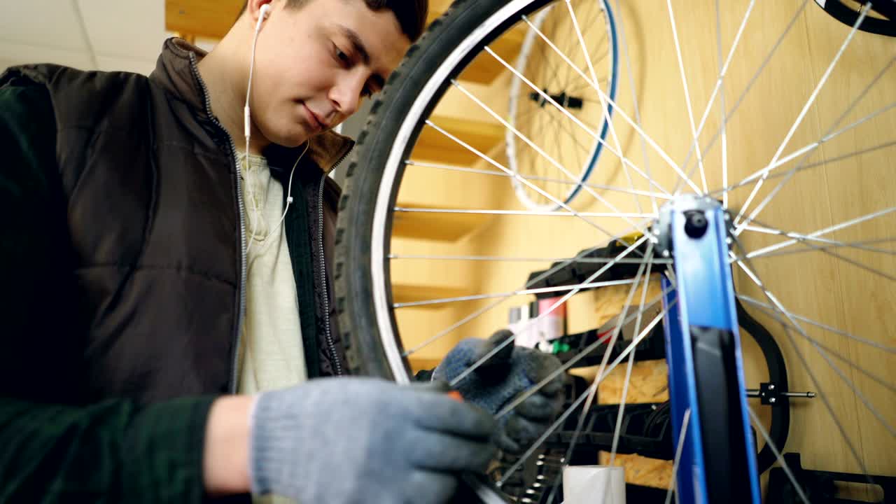 Professional repairman is fixing bicycle wheel spokes straightening them with special tools and rotating wheel to check spokes. Occupation and repair concept.