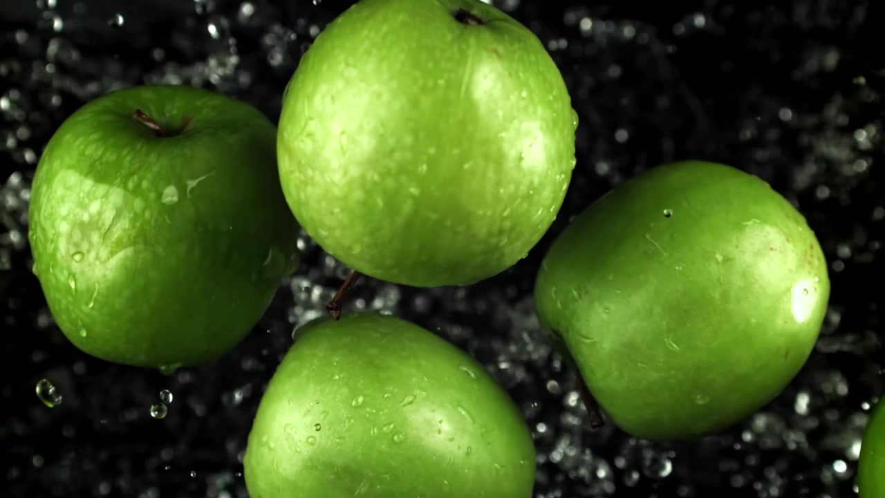 Mele verdi fresche con gocce d'acqua che schizzano su sfondo nero
