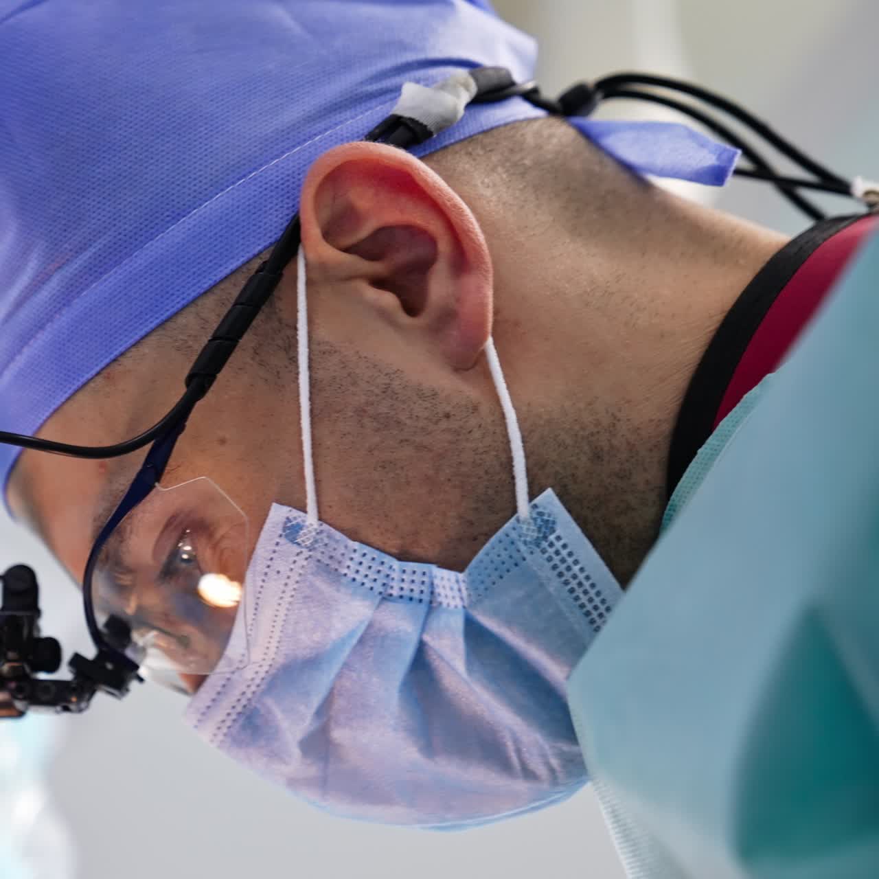 Medico con mascherina, cappello e occhiali con dispositivo speciale che opera in sala operatoria. Ritratto di un dottore durante un intervento chirurgico. Primo piano. Sfondo sfocato