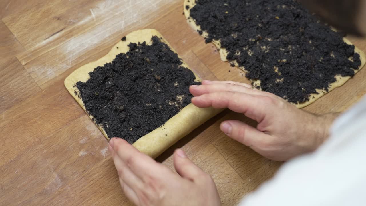 vista de arriba hacia abajo de las manos rodando la masa llena de semillas de amapola para crear la pastelería húngara de navidad bejgli