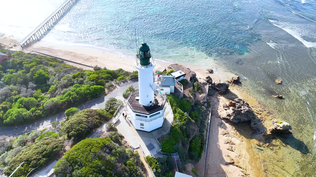 Aerial footage captures Point Lonsdale Lighthouse, lush greenery, and surrounding coastline under bright daylight
