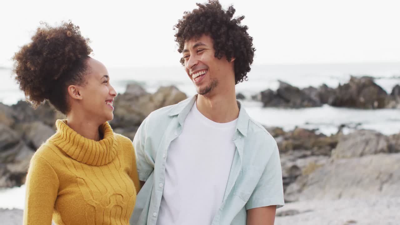 Retrato de casal afro-americano sorrindo em pé nas rochas à beira-mar.