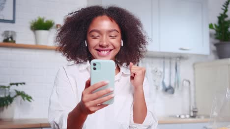 young joyful african american woman with phone in hand makes winning gesture