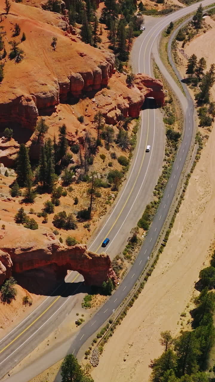 Cars going under the rock arches on the highway in National Park. Sunny daytime footage over the Arches canyons, Utah, USA. Vertical video