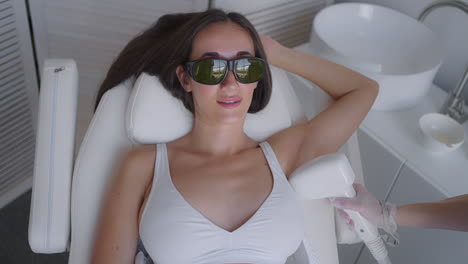 beautician-doing-armpit-laser-hair-removal-of-attractive-sexy-woman-lying-on-medical-couch-and-smiles-in-beauty-salon.-Cosmetologist-does-laser-hair-removal-of-armpits-of-patient.-Epilation-procedure