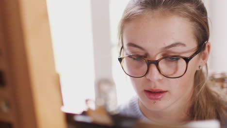 close up on face of female teenage artist working behind easel