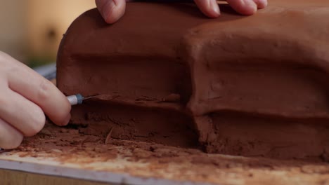 cerca de las manos del diseñador automotriz usando rastrillo o alambre para crear detalles en la escultura de arcilla de automóvil en el estudio