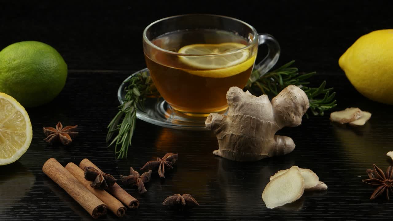 una taza de té, limón, lima, ramas de romero y especias para el té en una mesa de madera negra