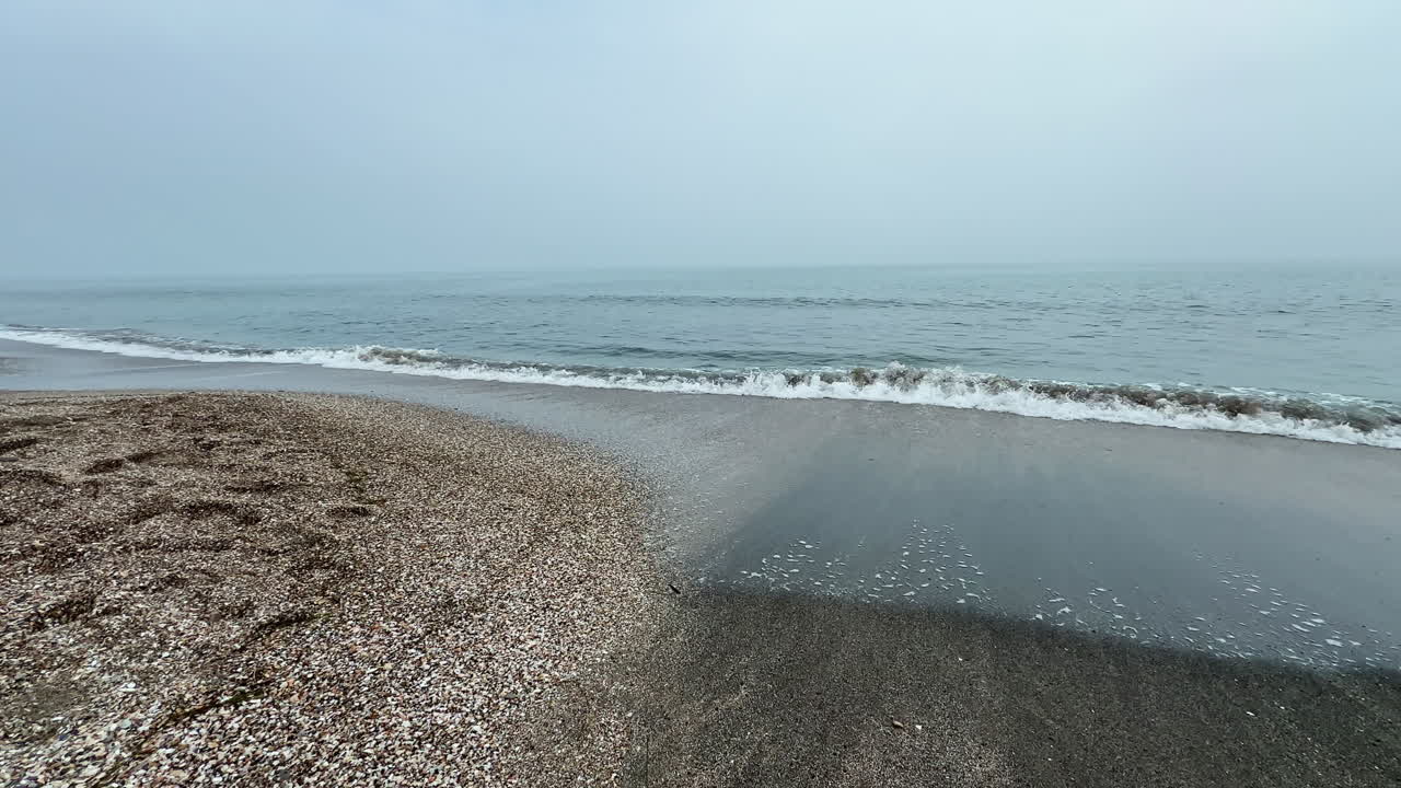 Cloudy sky over a quiet beach with wet sand and gentle waves rolling onto the shore at an early hour