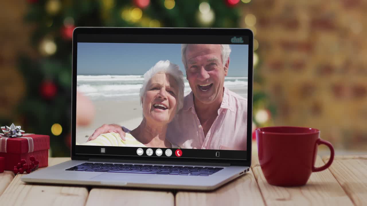 una pareja de alto nivel caucásica saludando en una videollamada en una computadora portátil, con un árbol de navidad